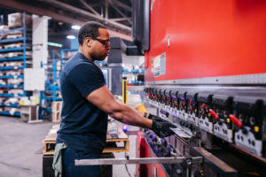 a man in a blue shirt operates a stamping press to create stamped metal components for welded commercial office furniture