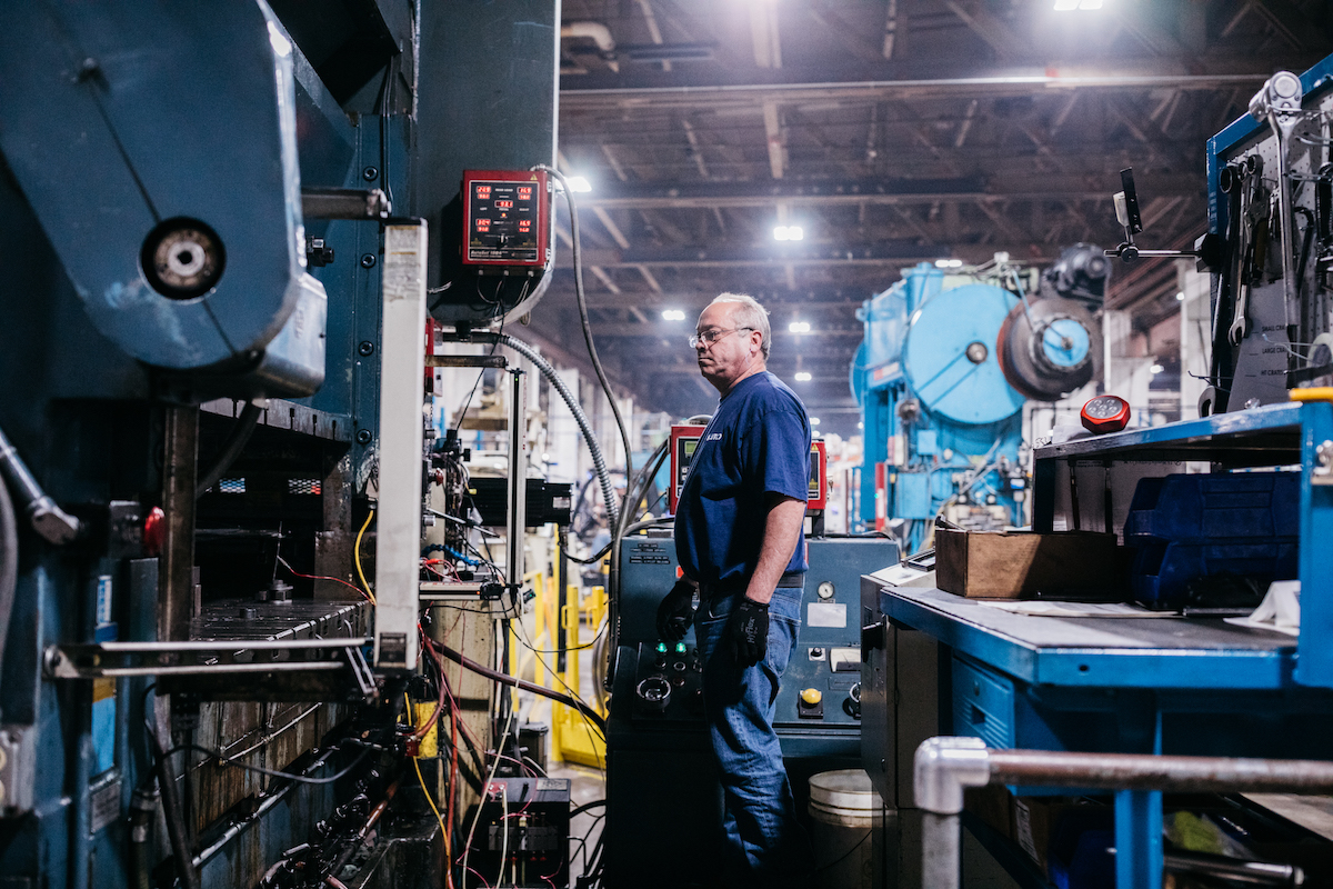 man in a blue shirt operating a blue press brake in a us-based manufacturing production floor