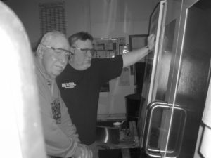 Rick LeBoeuf demonstrates a CNC machine for his father in a black and white image