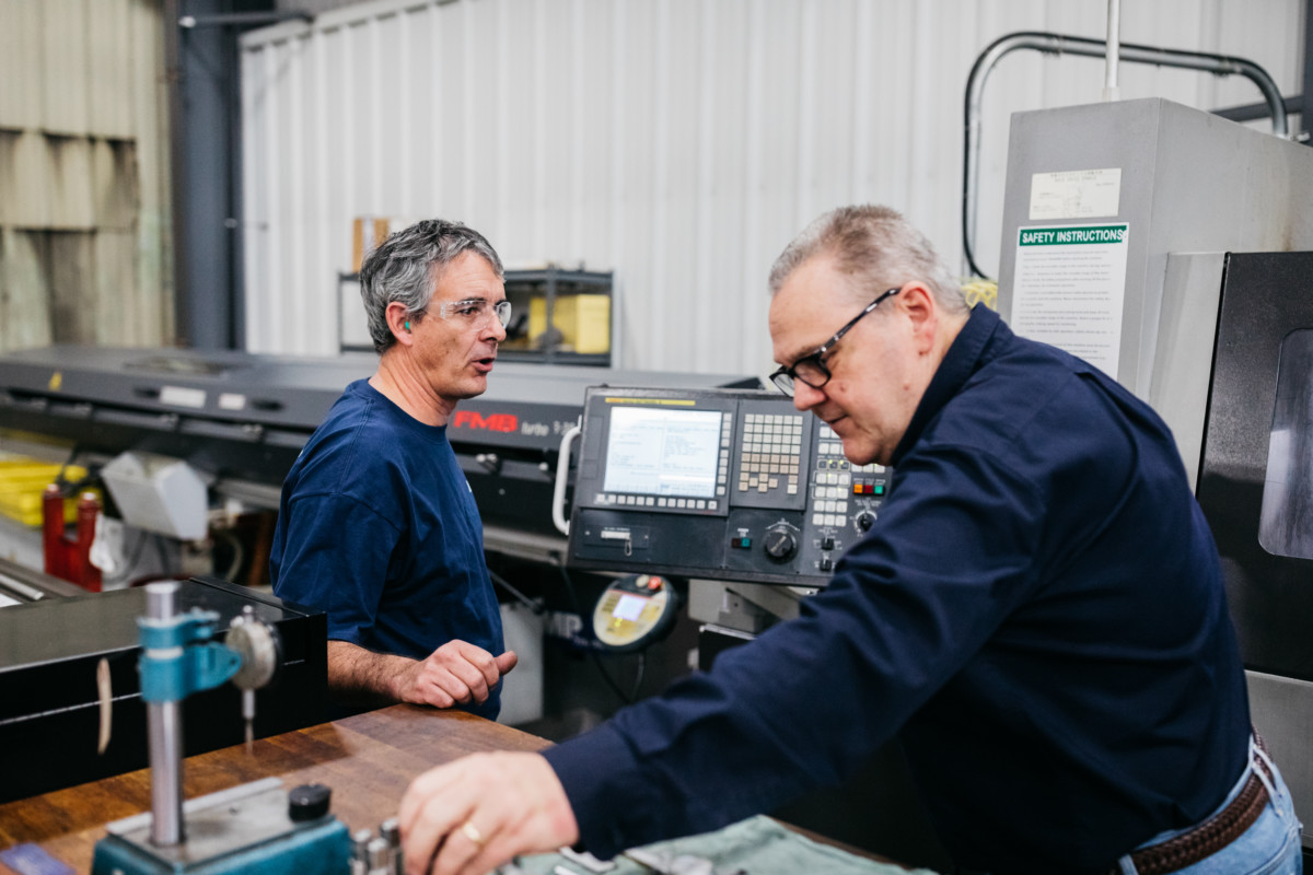 Two men in blue Lutco shirts using a CNC swiss turning machine.