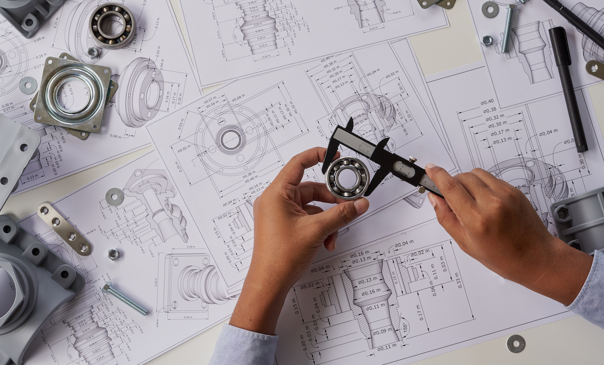 Two hands measuring a custom bearing with caliper tools.