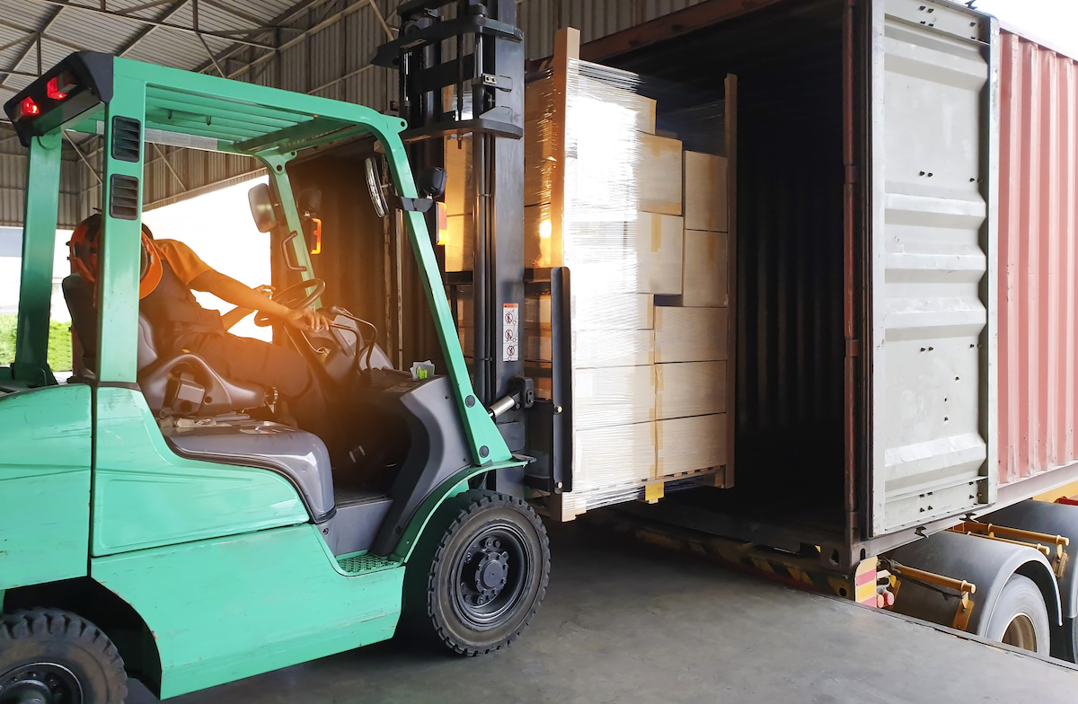 A forklift loading a locked freight truck at the loading dock of a shipping facility.