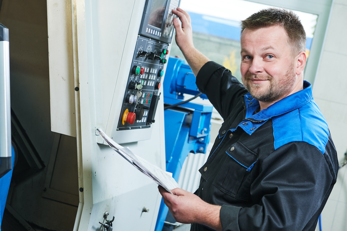 A man in a blue and black shirt operating a cnc machine in his manufacturing job.