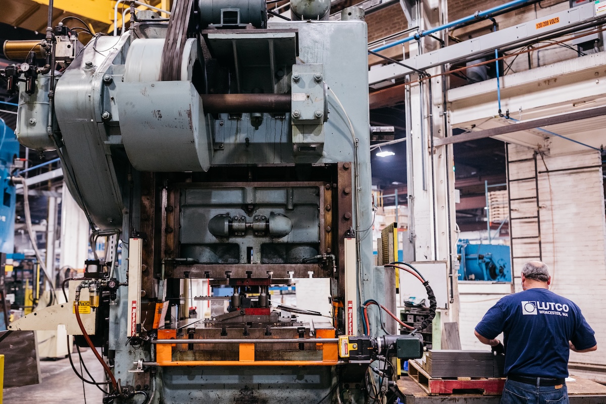 A Lutco employee in a blue shirt works a heavy stamping machine.